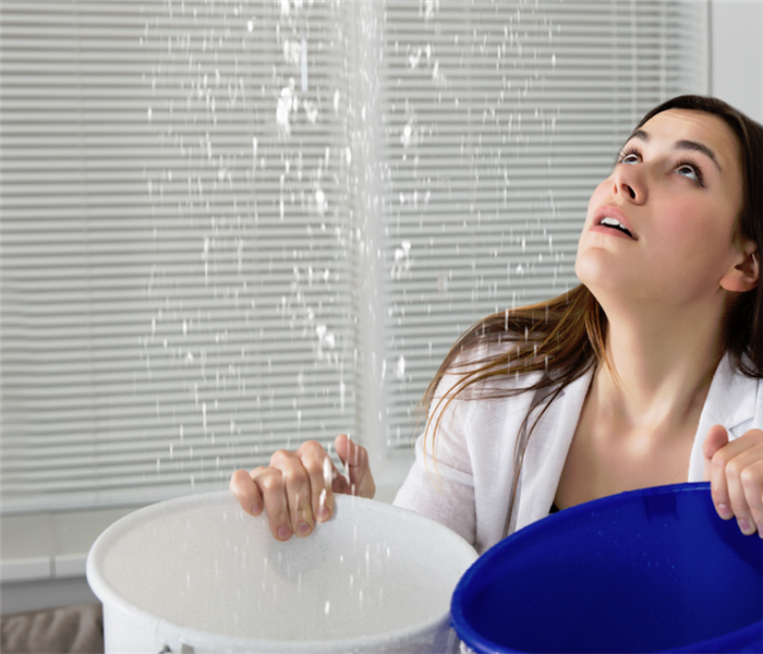 a woman holding buckets to catch water falling from the ceiling